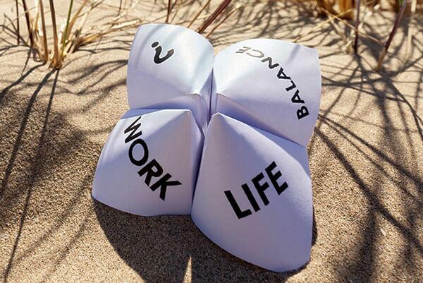 Ein Papierquader liegt im Sand mit den Worten Work, Life, Balance, ?